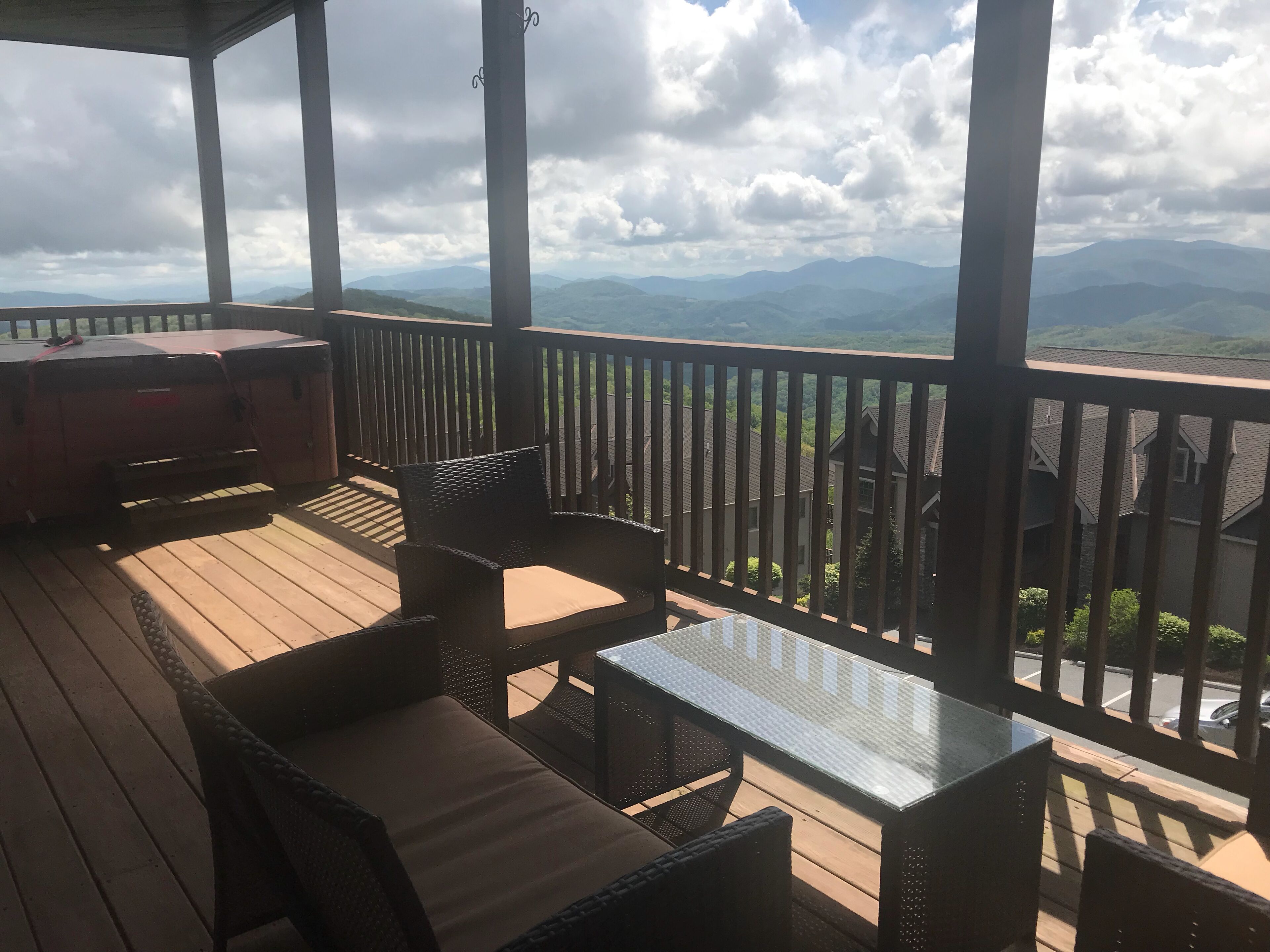 Eine überdachte Terrasse im Freien mit Korbmöbeln und einem Glastisch, mit Blick auf eine Berglandschaft.