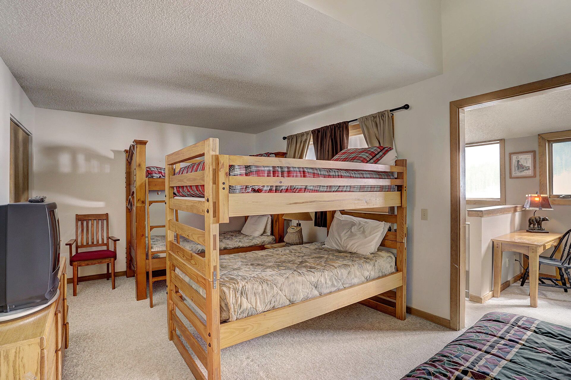 A bunk bed room with a television, a desk, and a chair.