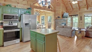 A spacious wooden cabin with a kitchen featuring a microwave, refrigerator, and stove, a dining area with a table and chairs, and a living room with a sofa and a television.