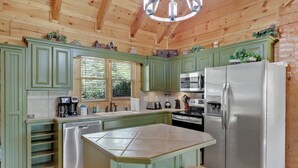 A kitchen with green cabinets, stainless steel appliances, and a central island with stools.