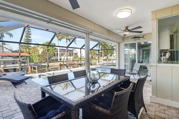 A glass-enclosed outdoor area with a pool, wicker furniture, and a ceiling fan.