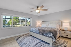 Un dormitorio con cama, mesitas de noche, ventilador de techo, ventana con vistas y alfombra.