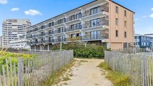 A multi-story building with balconies, a sandy pathway, and a wooden fence. - Direct Oceanfront Renovated Condo | Sunrise | Sleeps 8 (Ocean City)