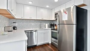 A modern kitchen with white cabinets, stainless steel appliances, a dishwasher, and a tiled backsplash. - Direct Oceanfront Renovated Condo | Sunrise | Sleeps 8 (Ocean City)