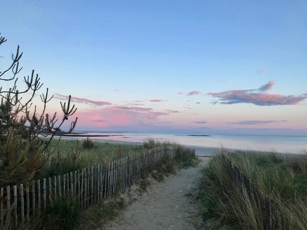 A sandy path leading to a beach with a wooden fence on one side.