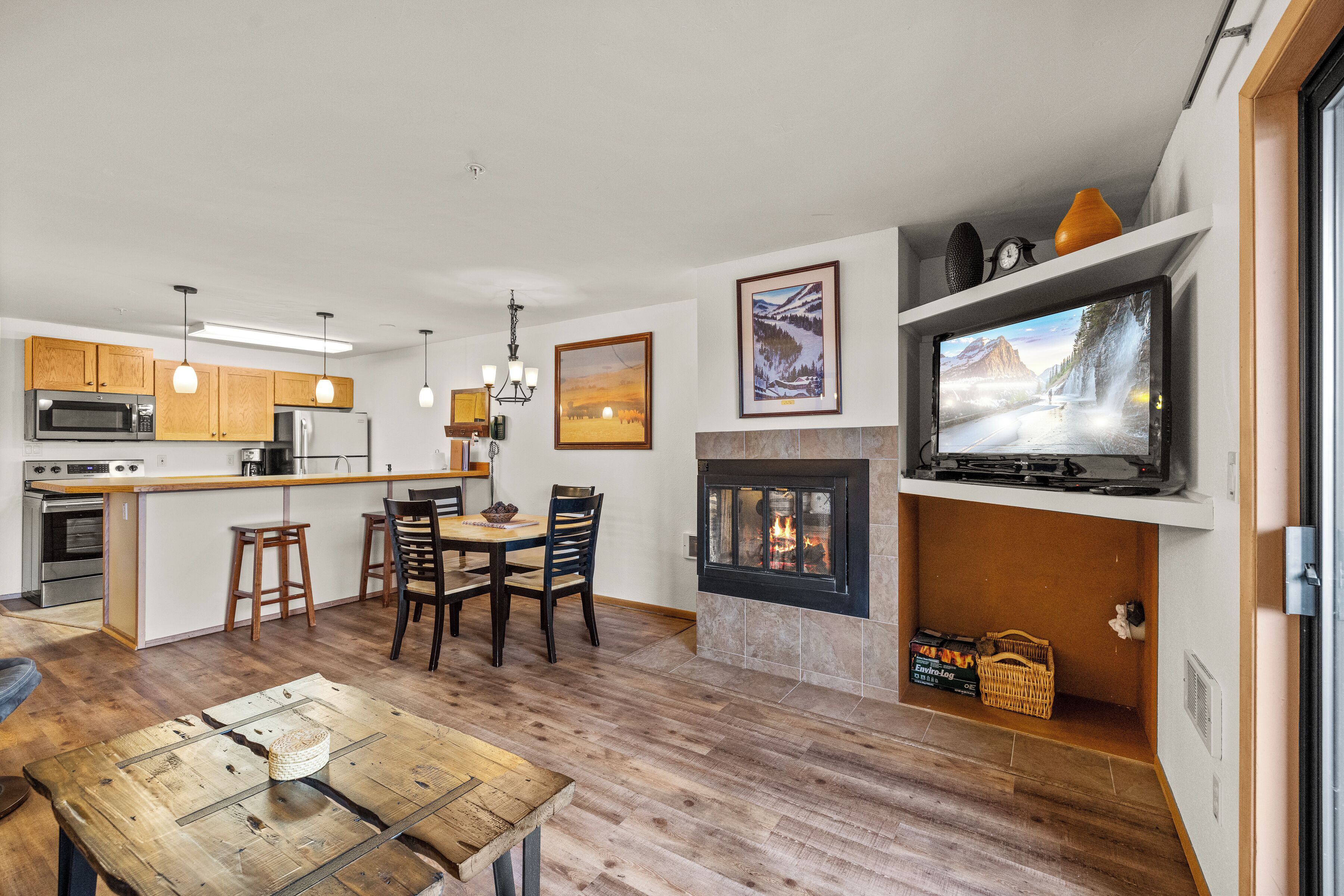 Una cocina moderna con armarios de madera, una isla central y una zona de comedor con mesa y sillas de madera.