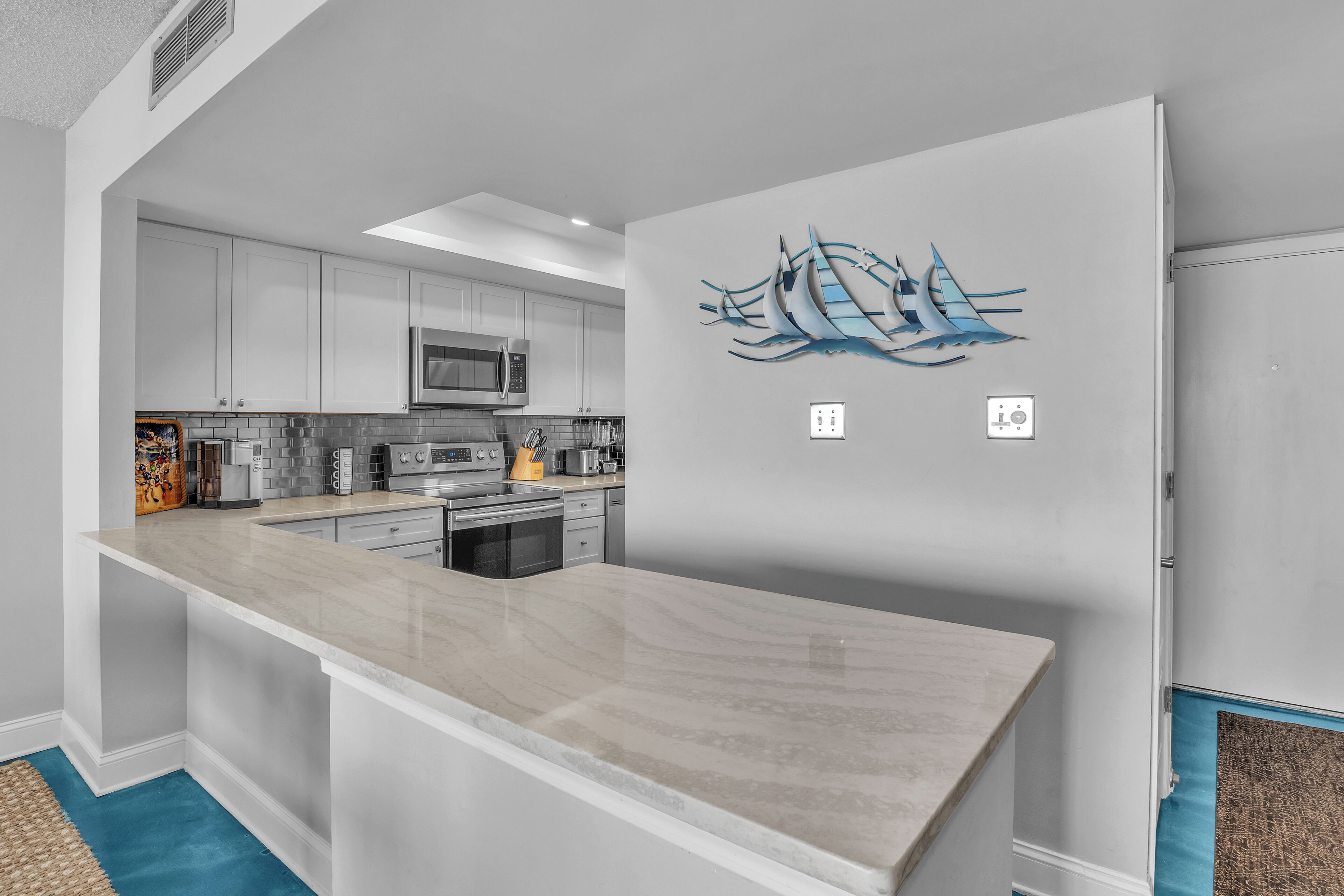 A modern kitchen with white cabinets, a marble countertop, and a wall-mounted microwave.