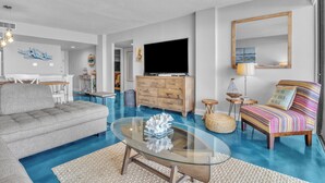Una sala de estar moderna con un sofá modular, una mesa de centro de vidrio, un televisor y un sillón colorido.