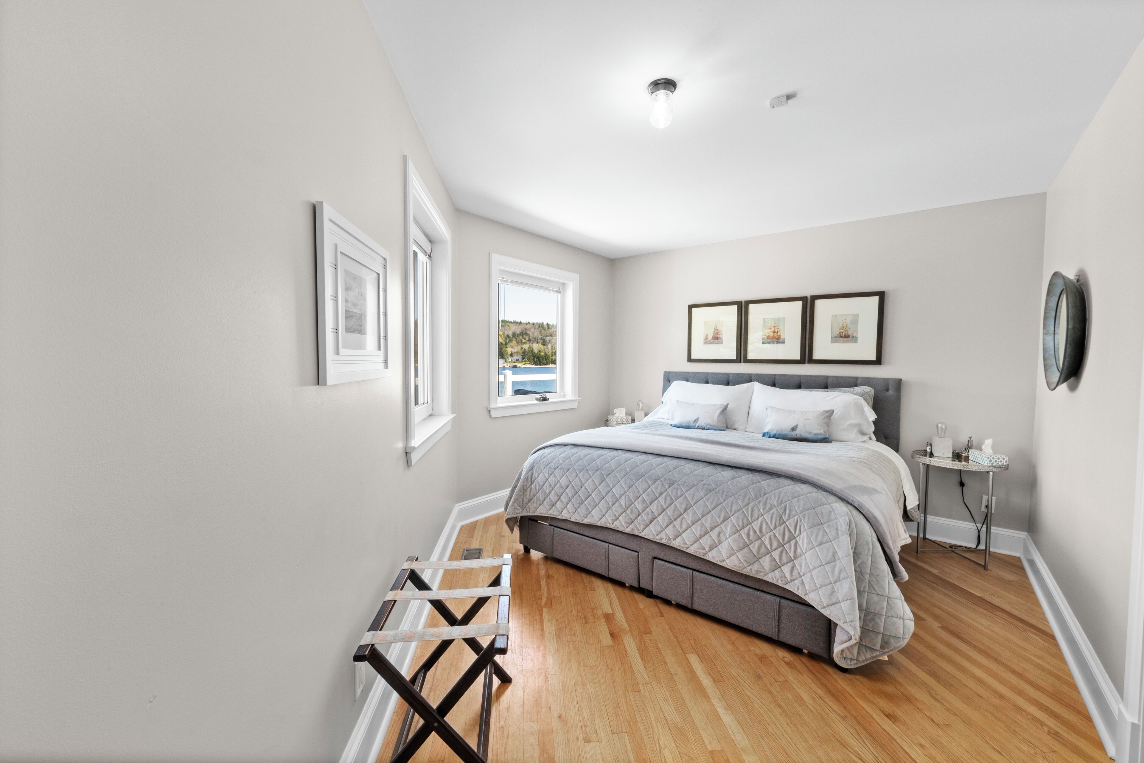 A bedroom with a bed, a window, a bedside table, and a wall-mounted picture.