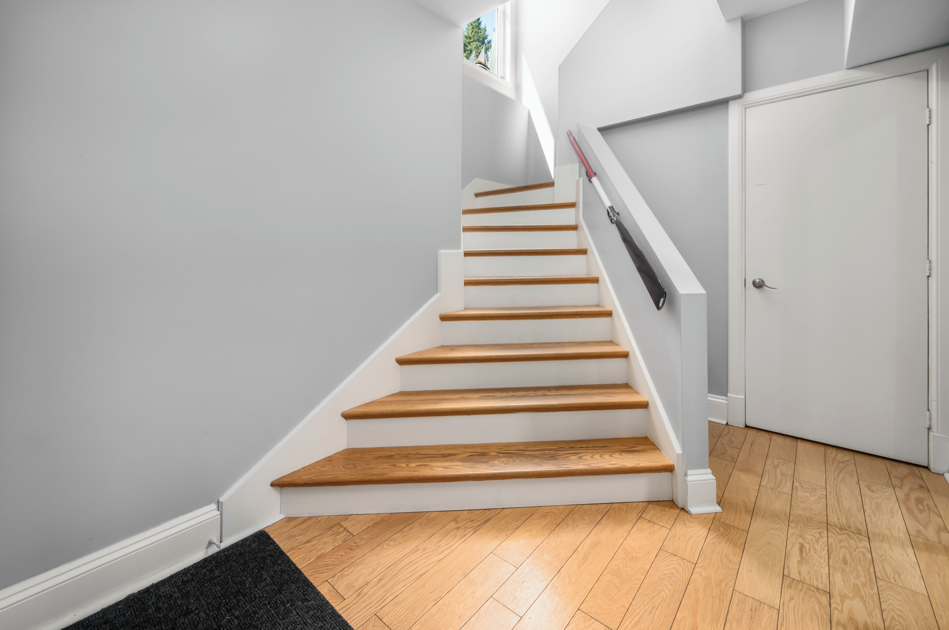A staircase with wooden steps and white walls, leading to a door.