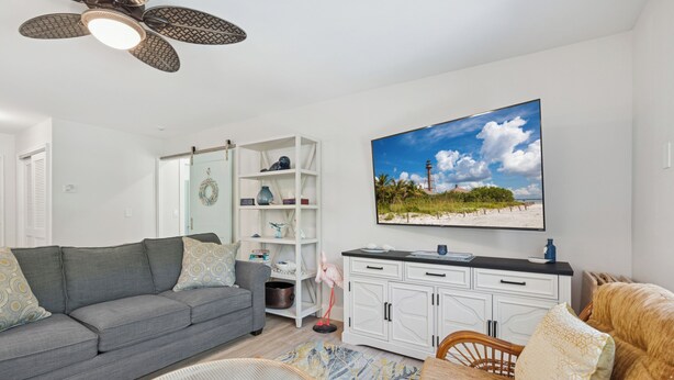 A living room with a grey sofa, a wicker chair, a white cabinet, and a painting of a beach scene.