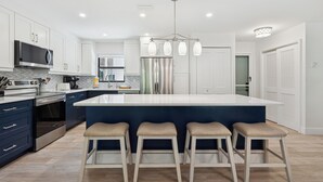 A modern kitchen with white cabinets, stainless steel appliances, a central island with bar stools, and pendant lighting.