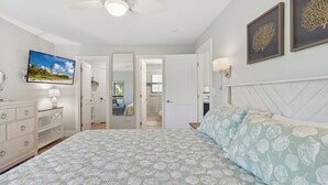 A bedroom with a bed, dresser, TV, and artwork.
