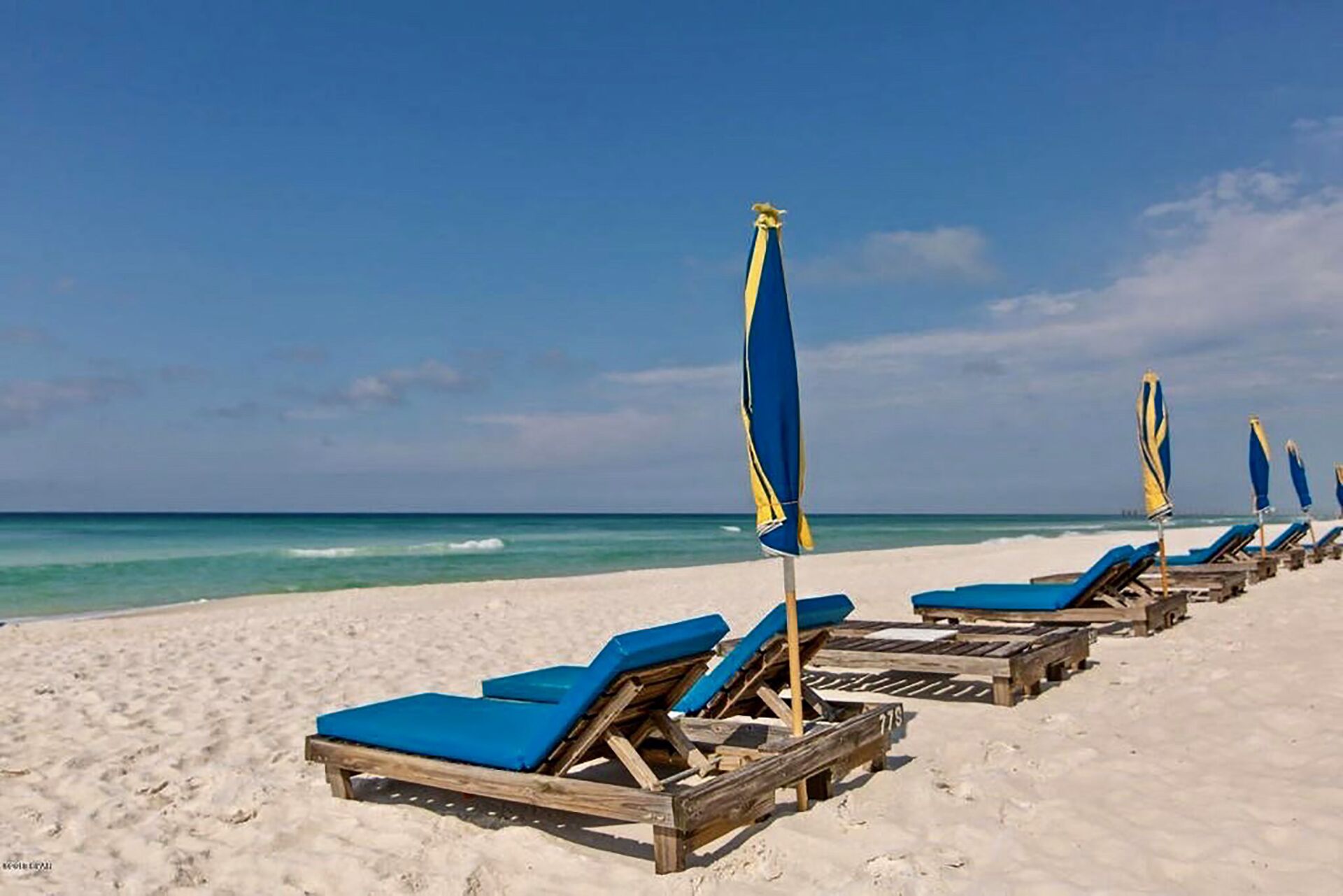 Una playa con sillones de madera y sombrillas azules.