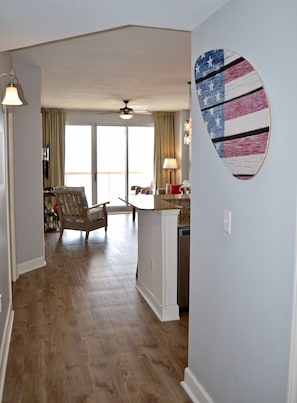 A spacious living room with a wooden floor, a ceiling fan, and a view to the outside.