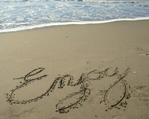 Ein Strand, auf dem das Wort 'Enjoy' in den Sand geschrieben steht.