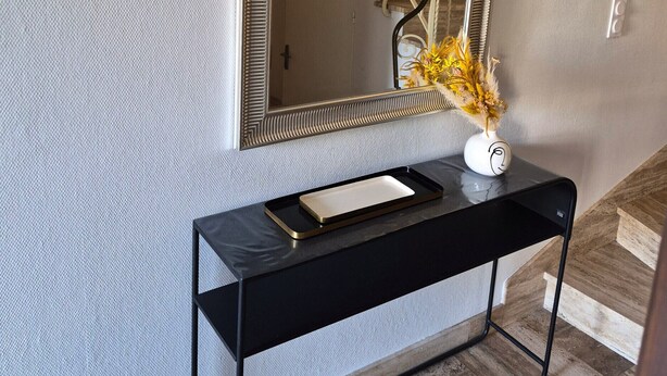 Ein modernes Interieur mit einem schwarzen Konsolentisch, einer dekorativen Vase und einem großen Spiegel, der eine Treppe reflektiert.