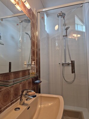 Une salle de bain avec une douche à parois de verre, un lavabo beige et un miroir avec un pare-éclaboussures en bois.