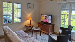 Ein Wohnzimmer mit einer Couch, einem Fernseher, einer Lampe und einem Korbstuhl.