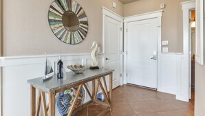 A hallway with a round mirror, a seahorse sculpture, and a table with a bottle and a bowl.