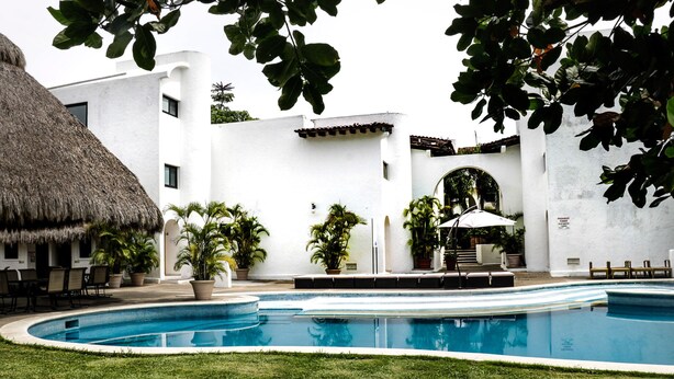 A swimming pool with a thatched roof structure, surrounded by white walls and potted plants. - Marina Golf Condo in the heart of the Marina Vallarta (Marina Vallarta)