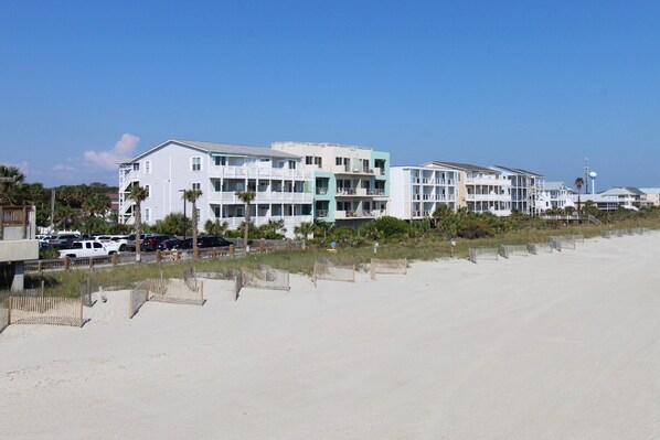 A beachfront hotel with multiple balconies, a parking area, and a sandy beach.