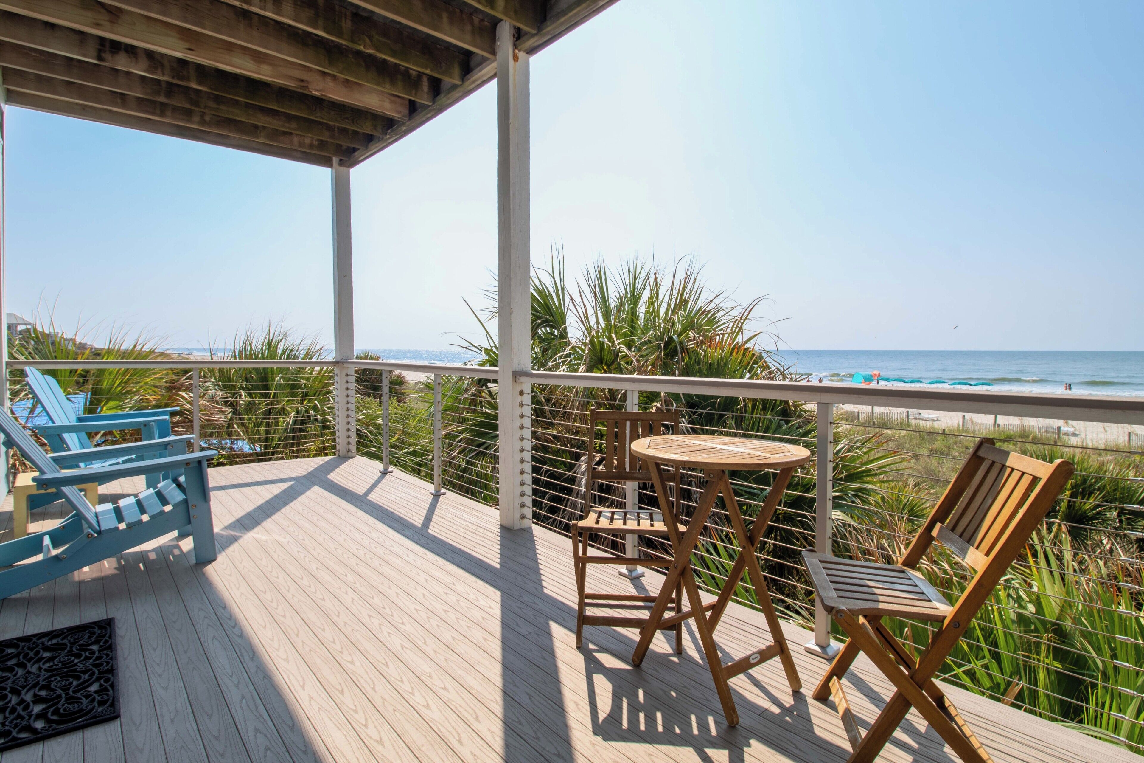 A wooden deck with a view of the ocean, featuring a table and chairs, and a railing.