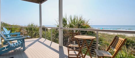 A wooden deck with a view of the ocean, featuring a table and chairs, and a railing.