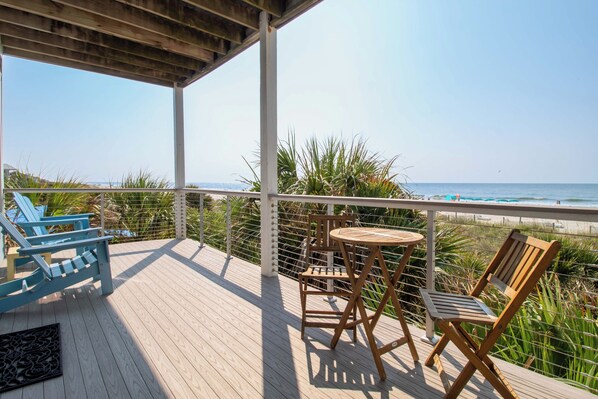 A wooden deck with a view of the ocean, featuring a table and chairs, and a railing.