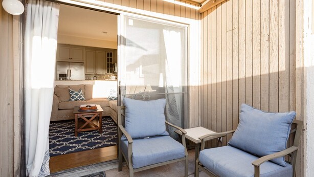 Een balkon met twee stoelen, een kleine tafel en een bank met een kamerkleed met patroon.