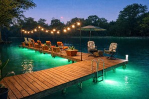 A wooden dock extending into a body of water, with lounge chairs and a table under string lights. - Huge Riverfront House, Sleeps 32, 11BR, 6BA, 70' Pier (McQueeney)