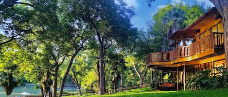 A wooden cabin with a balcony, surrounded by lush greenery and trees.