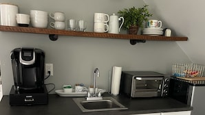 A modern kitchen with white cabinetry, a black coffee maker, a toaster, and a sink. - King's Country Suite (Narvon)