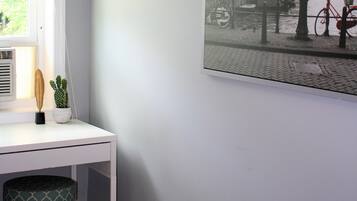 Una stanza con una scrivania bianca, una finestra con persiane, un cactus e un quadro che raffigura un canale.