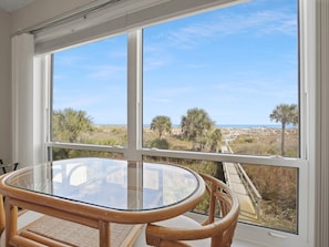 A room with a large window offering a view of the beach and palm trees. - Oceanfront condo with beautiful ocean view and screened patio- SO 4 (St. Augustine Beach)