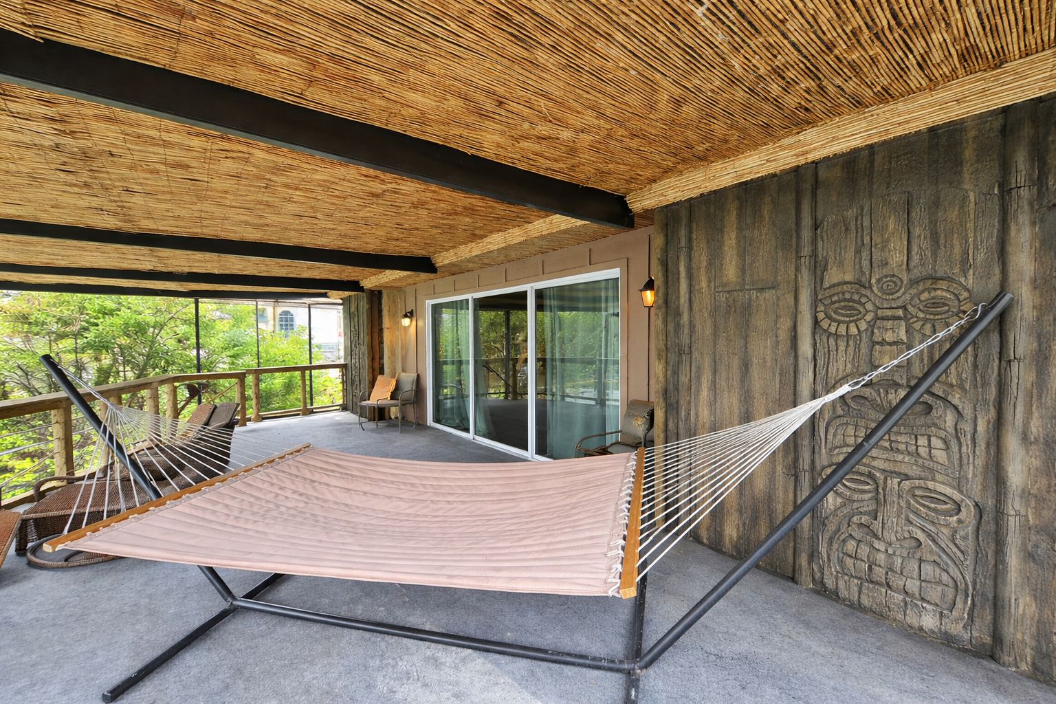 A hammock on a balcony with a wooden ceiling and a stone wall with carvings.