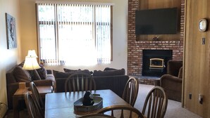 A living room with a dining table, chairs, a sofa, a TV mounted on the wall, and a fireplace. - Pet friendly, newly updated, 2 bedroom and a loft woodlands unit (Mammoth Lakes)