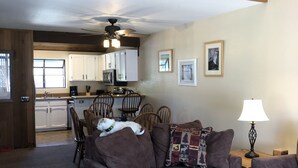 A spacious living room with a brown sofa set, a wooden coffee table with a bear sculpture, and a dining area with wooden chairs and a kitchen in the background. - Pet friendly, newly updated, 2 bedroom and a loft woodlands unit (Mammoth Lakes)