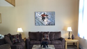 A living room with a wooden coffee table, two sofas, a bear figurine, and a painting of a skier. - Pet friendly, newly updated, 2 bedroom and a loft woodlands unit (Mammoth Lakes)