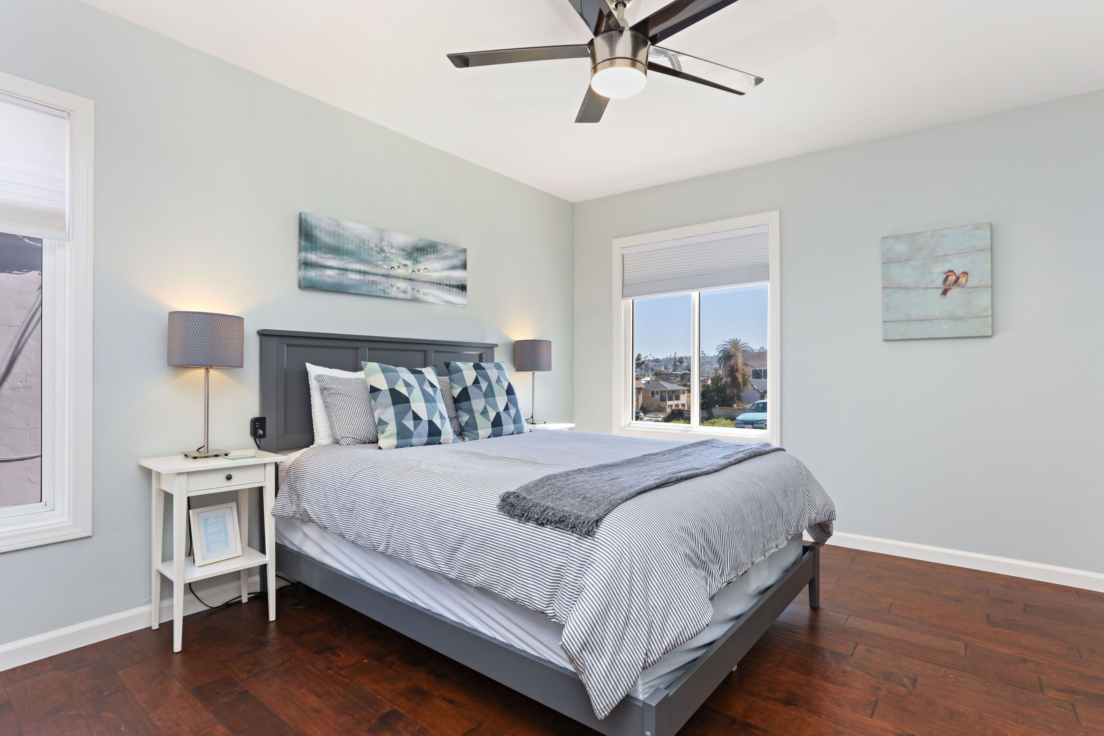 A bedroom with a bed, nightstands, a ceiling fan, and artwork on the walls.