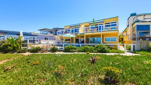 Un bâtiment à deux étages doté de balcons, un jardin agrémenté de diverses plantes et un ciel d’un bleu éclatant.