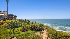 Une propriété située sur la côte, avec un sentier menant à l’océan, entourée d’une végétation luxuriante et offrant une vue dégagée sur la mer.