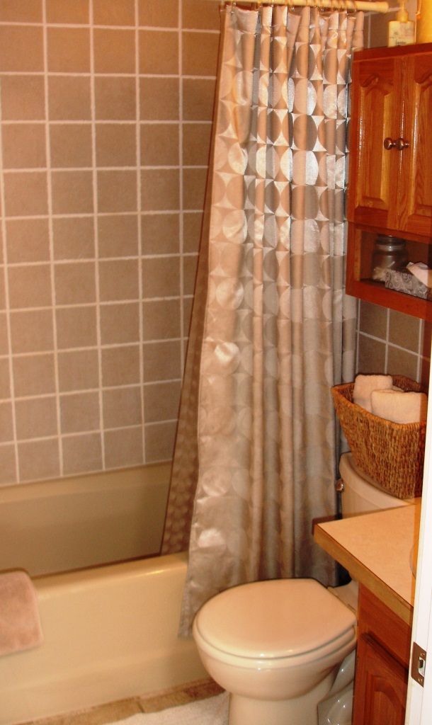 A bathroom with a toilet, a shower curtain, a tiled wall, and a wooden cabinet with a basket of towels.