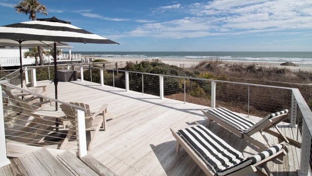Une terrasse en bois avec des chaises longues et vue sur la plage.