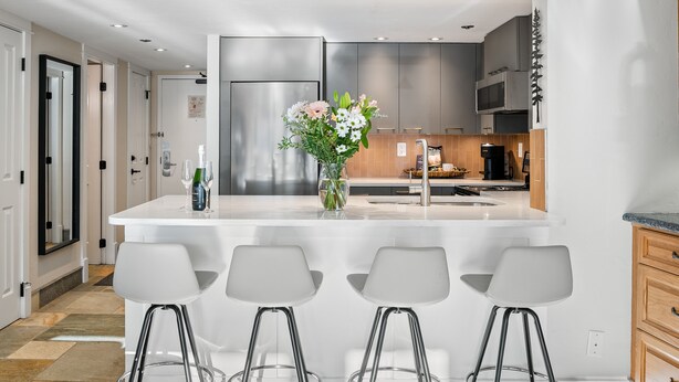 Una cucina moderna con isola centrale, sgabelli da bar e un vaso di fiori.