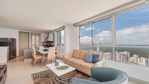 A modern living room with a large window, a sofa, a dining table, and a kitchen area. - Spectacular 2BR with Unbeatable View in Palmetto Beach (Cartagena)
