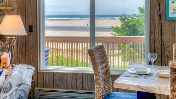 Una habitación con vista a la playa, una mesa de comedor con una copa de vino y una silla de mimbre.