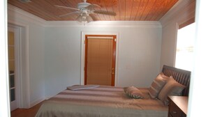 Une chambre à coucher avec un lit, une commode, un ventilateur de plafond et une porte.