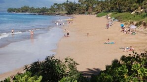 A beach with people sunbathing and swimming, surrounded by palm trees and a clear sky. - Rare, Spacious Penthouse, Big Ocean and Mountain Views, Great Location,  AC (Maui)