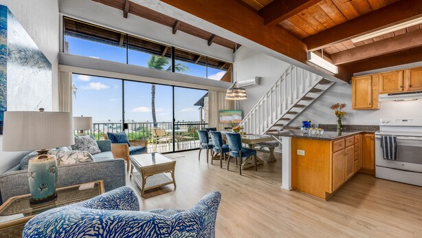 A spacious living area with a large window, a dining area, and a kitchen with wooden cabinets and a built-in oven. - Rare, Spacious Penthouse, Big Ocean and Mountain Views, Great Location,  AC (Maui)